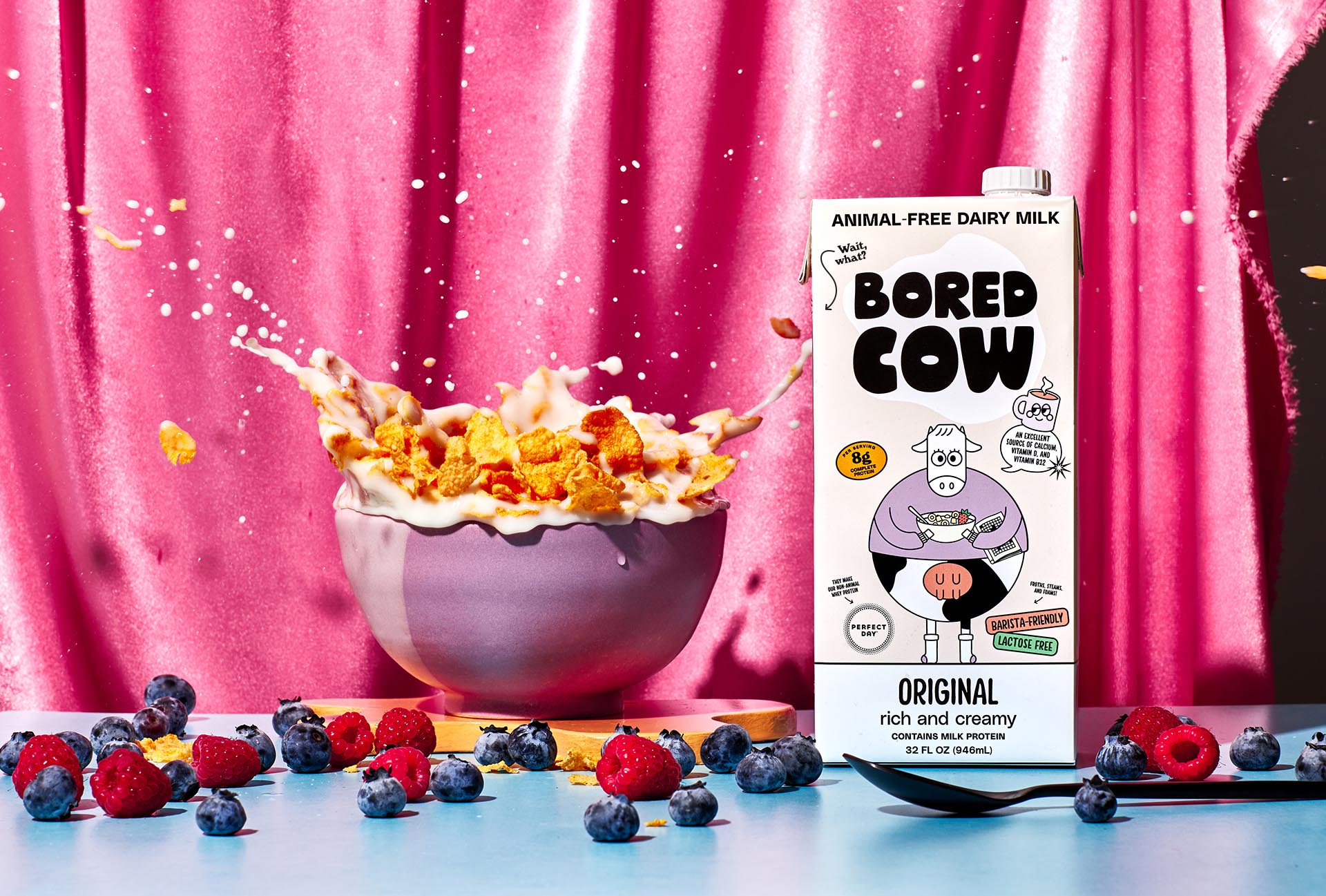 bowl of cereal with milk splashing out of it, to the right is a 32 oz carton of Bored Cow Original flavor animal-free dairy milk